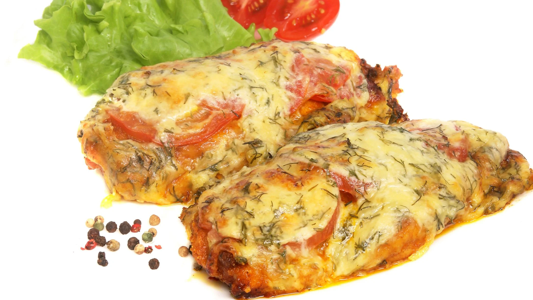 Two baked chops topped with melted cheese, tomatoes, and herbs, served with lettuce and a halved tomato.