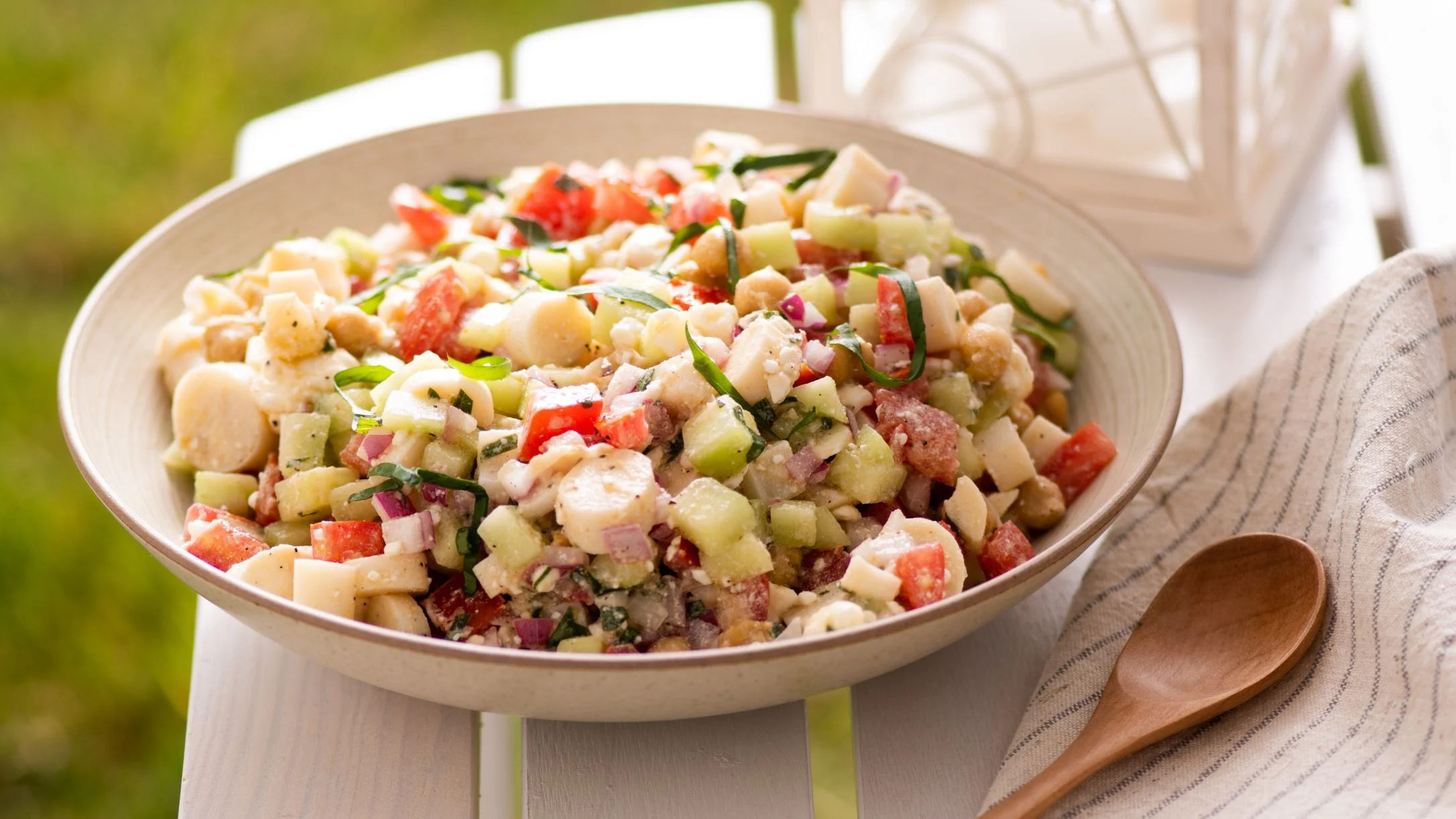 Fresh chickpea salad with diced vegetables, herbs, and red onion in a cream-colored bowl with wooden spoon nearby.