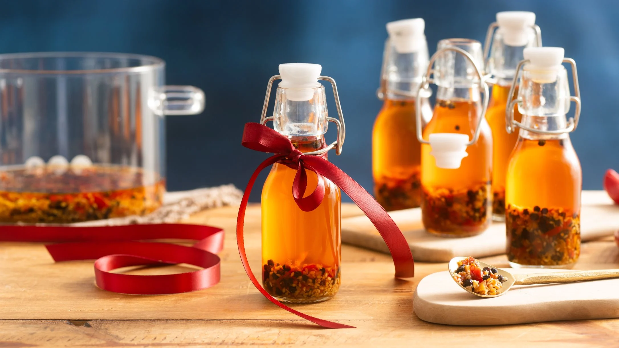 Small glass bottles of homemade infused oil with herbs and spices, one tied with a red ribbon, on wooden surface.