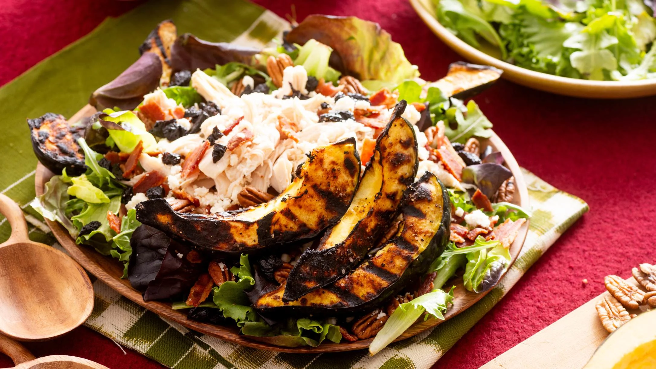 A wooden plate with a salad topped with grilled acorn squash, shredded chicken, pecans, bacon, and mixed greens.