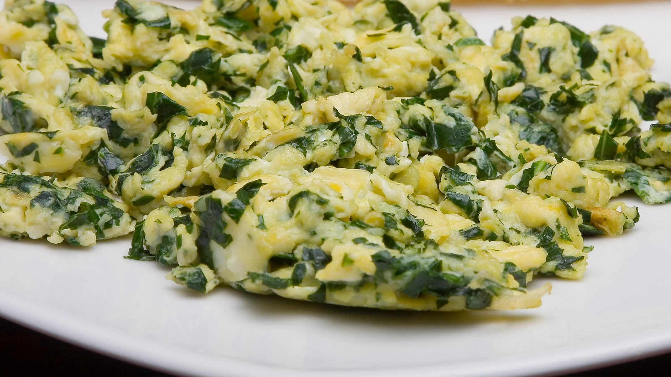 Scrambled eggs mixed with chopped green spinach, served on a white plate, showing a yellow and green color combination.