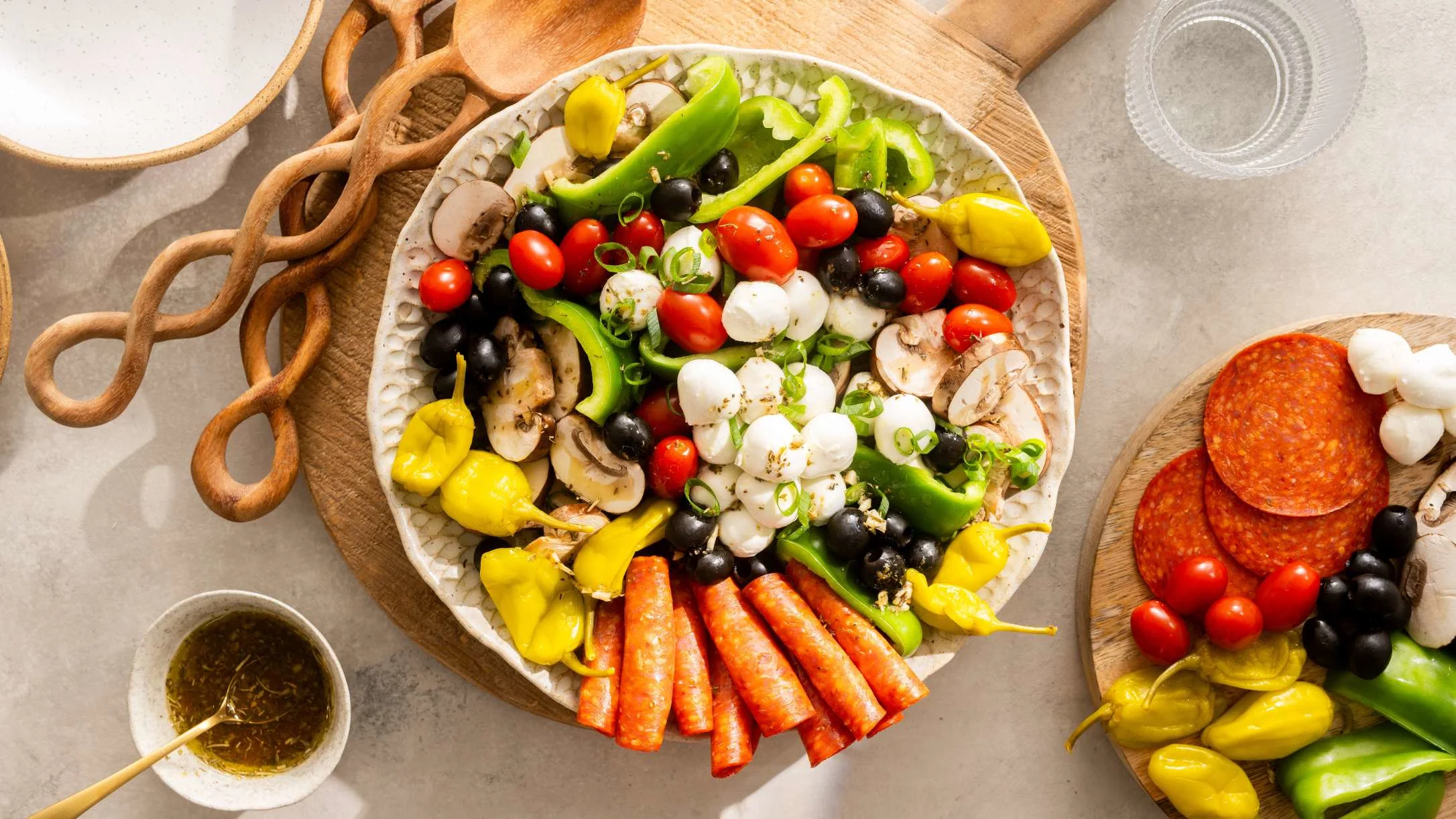 A colorful antipasto salad bowl with pepperoni, mozzarella, tomatoes, olives, peppers, and mushrooms on a wooden board.