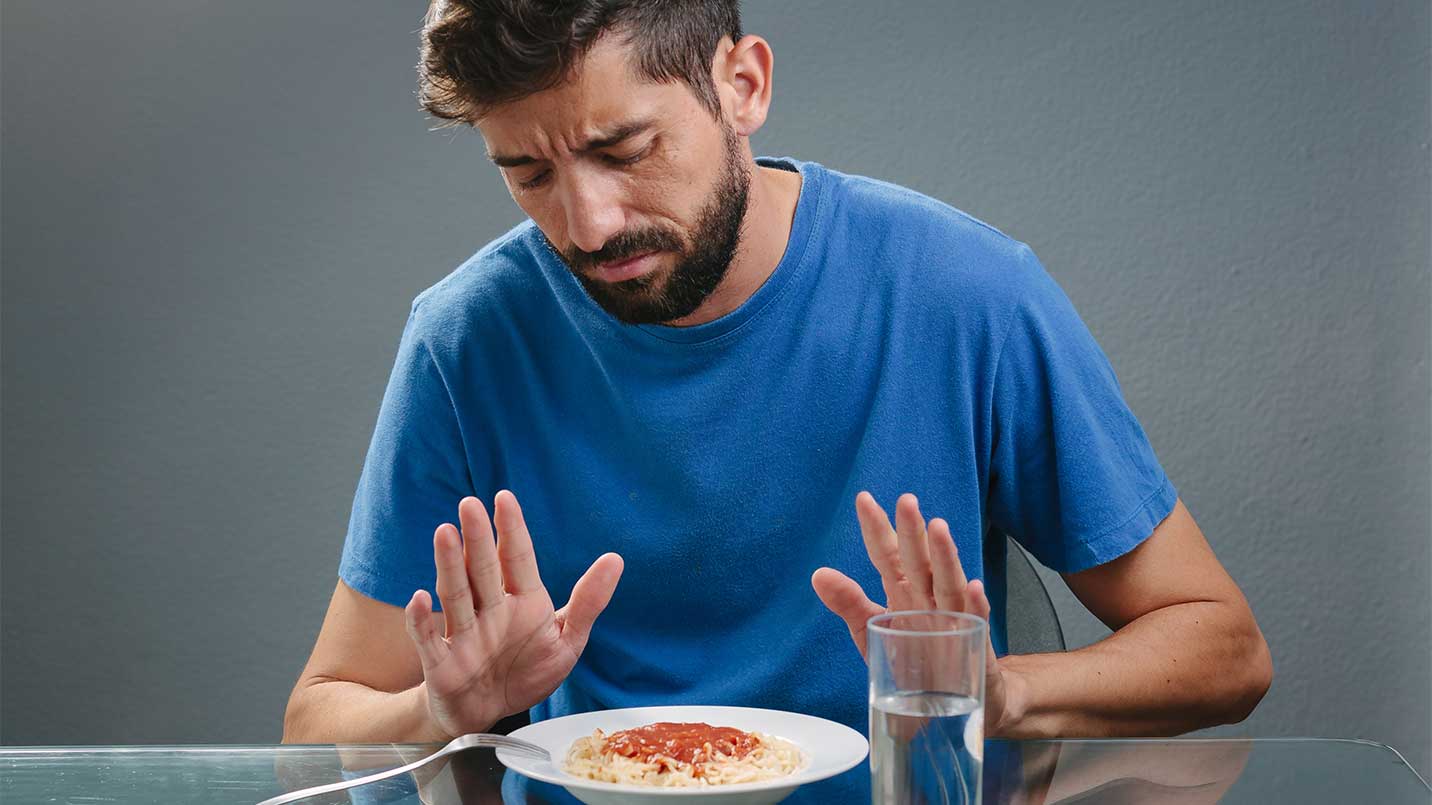 man showing discomfort and refusing a spaghetti dinner because of lack of appetite