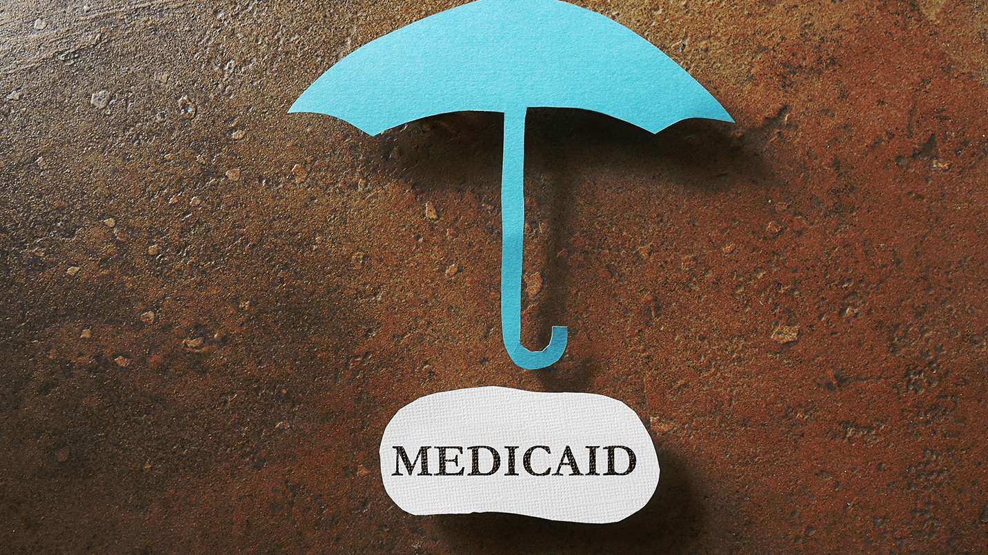 the word "medicaid" typed on a small piece of paper under a blue paper umbrella