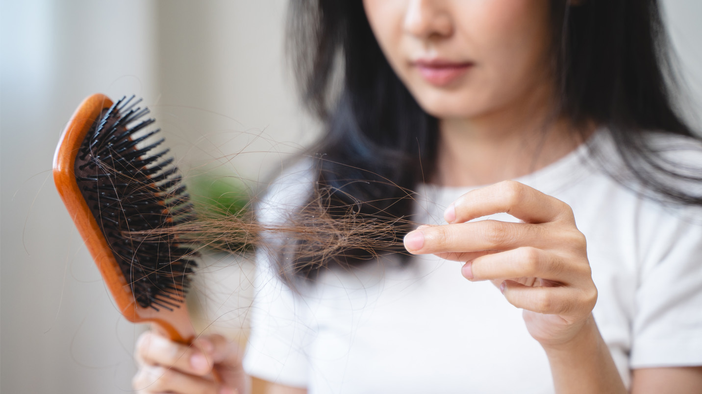 Woman holding brush and pulling clump of hair from the brush