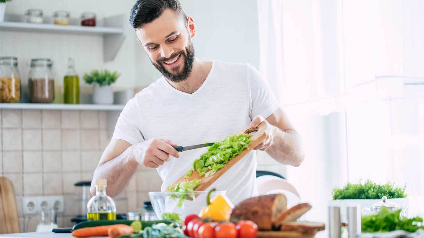 man with a beard smiling and cutting up vegetables in a kitchen