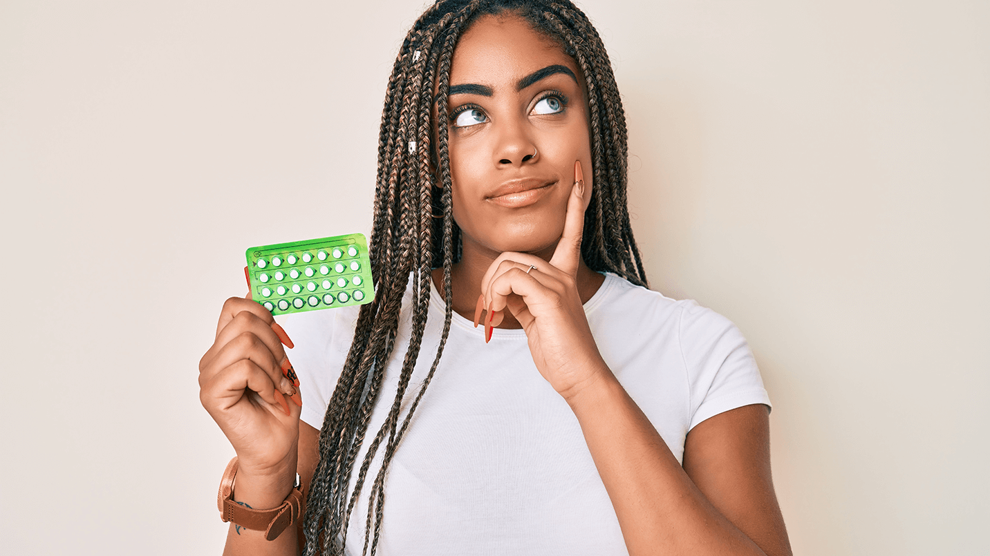 young black female holding a pack of birth control pills looking thoughtful