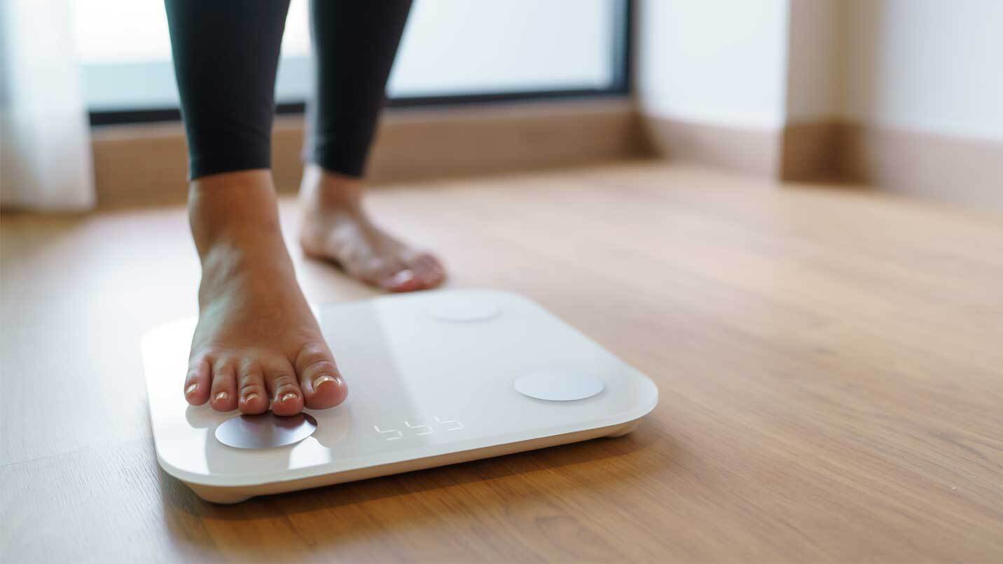 woman stepping on a white weight scale