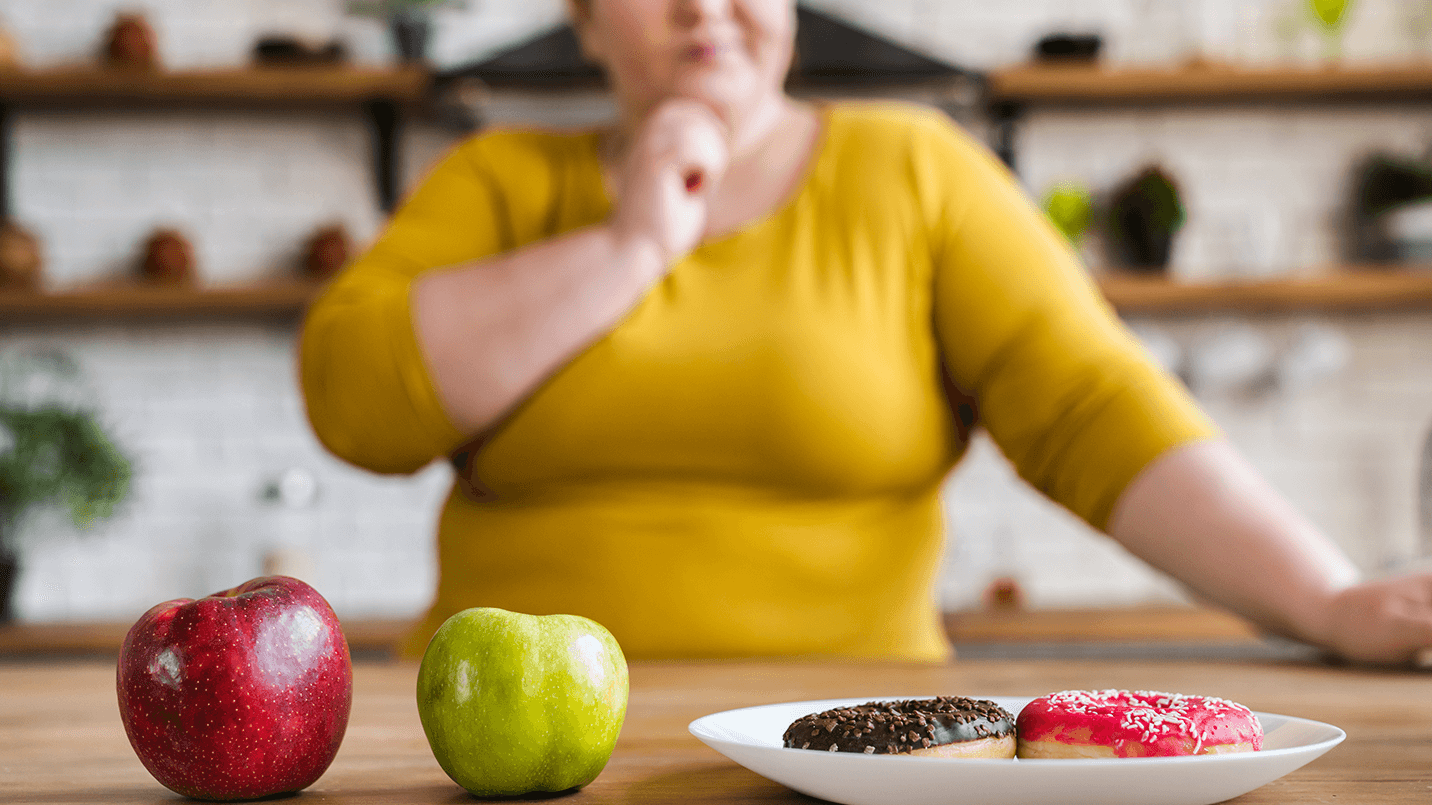 woman wearing yellow choosing between a health apple or a sugary donut