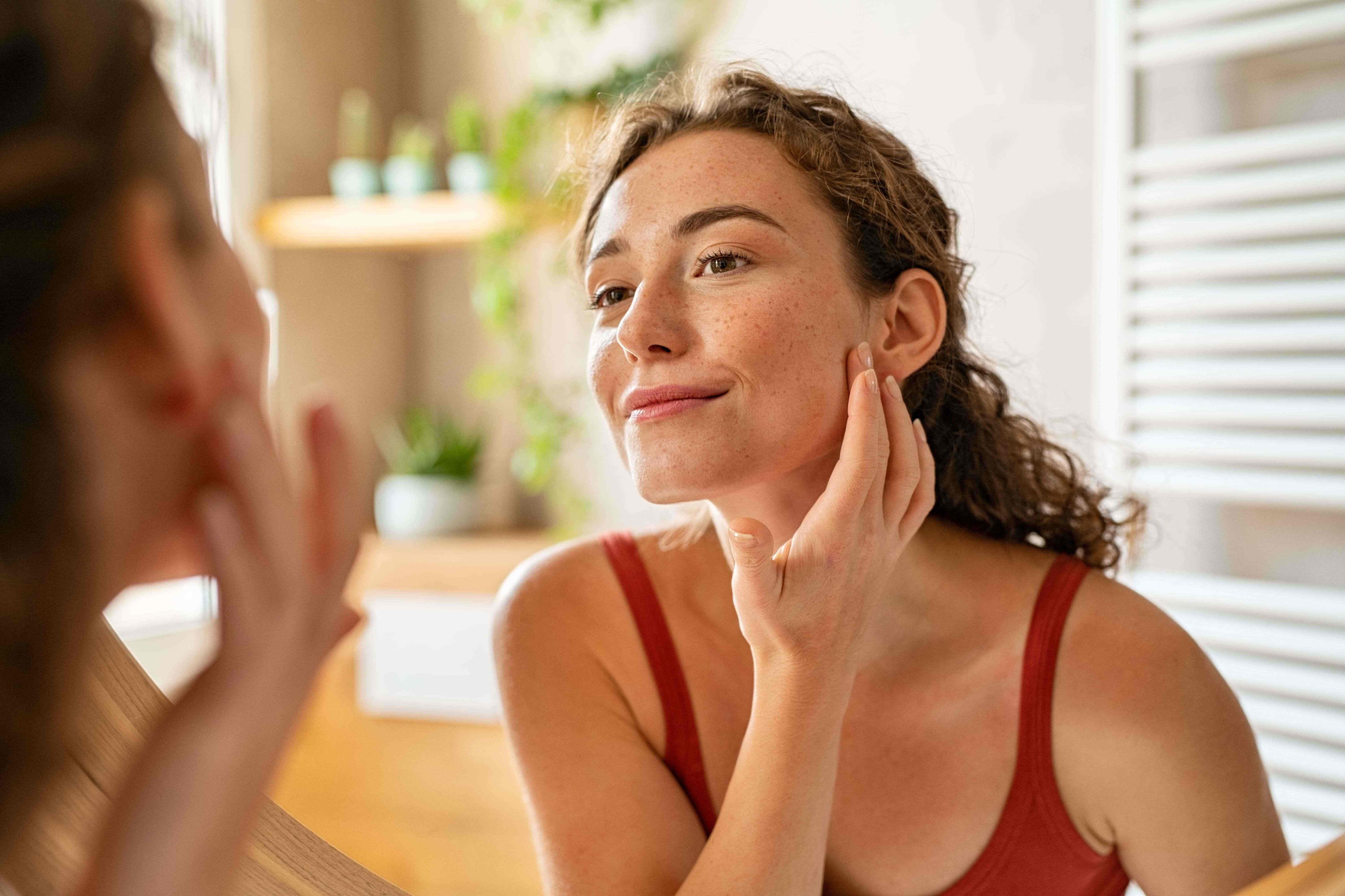 Young woman looking at her acne in the mirror.