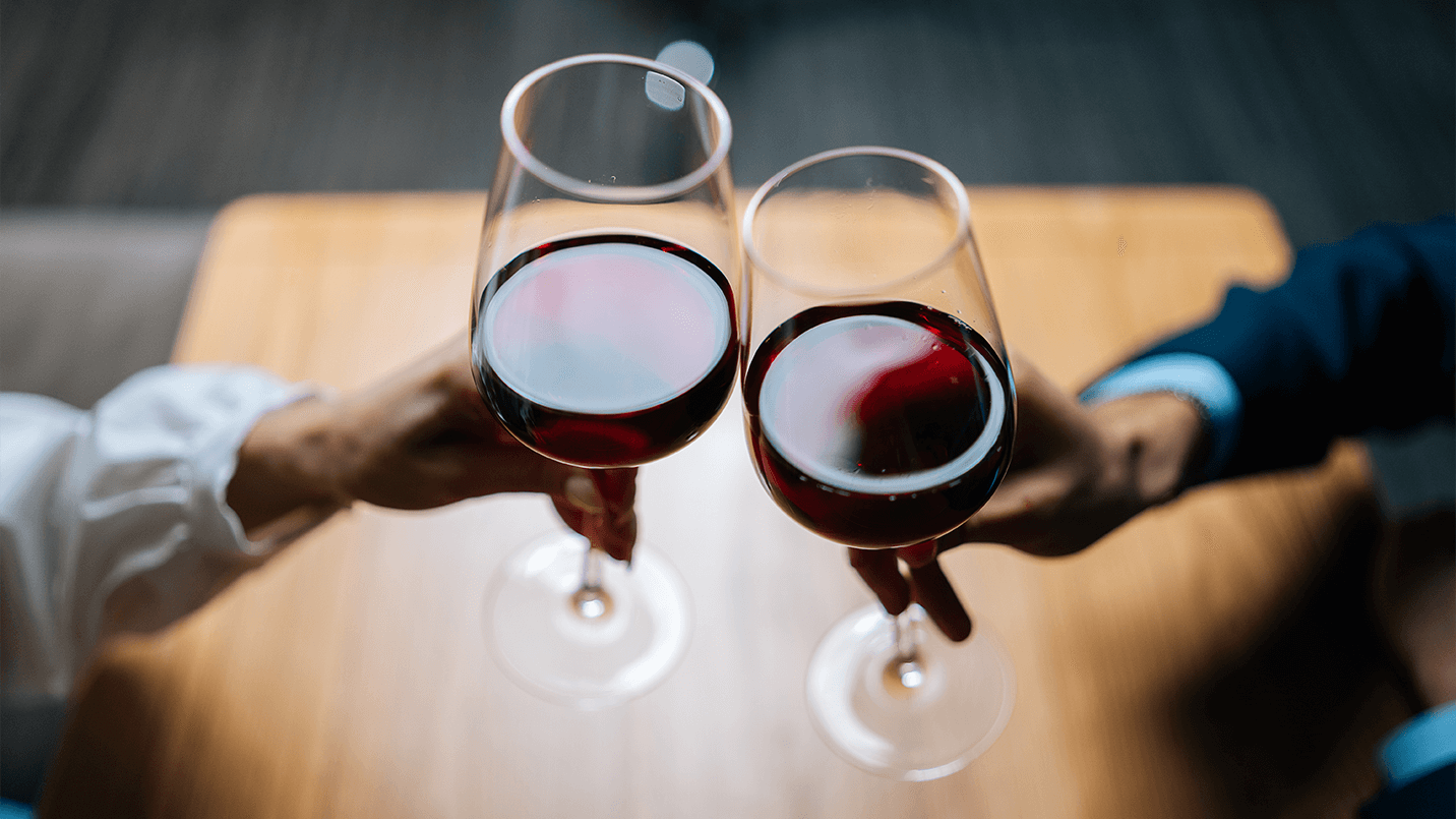 a woman and man clink their glasses full of red wine