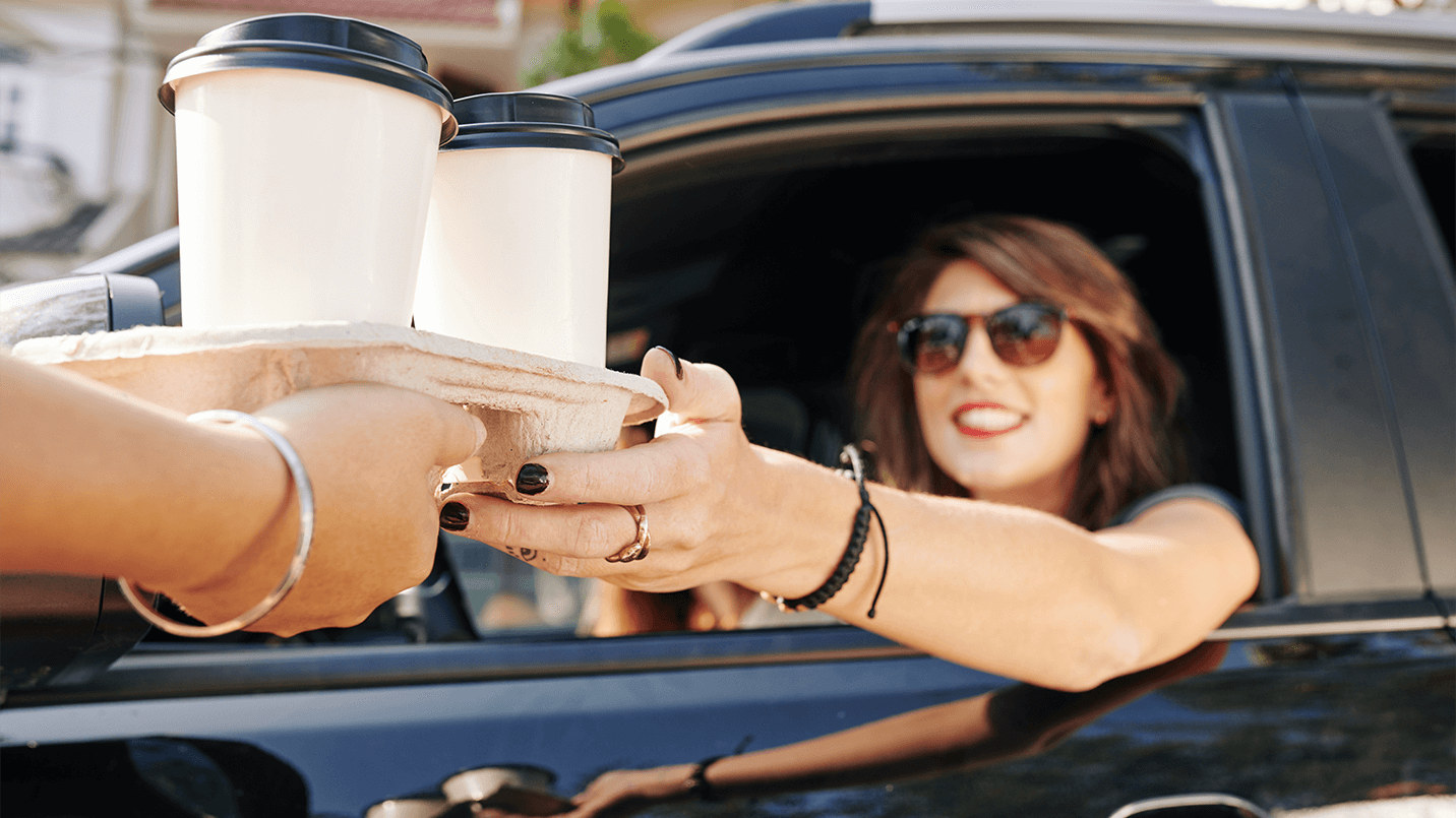 woman in her car being handed coffee from drive through window