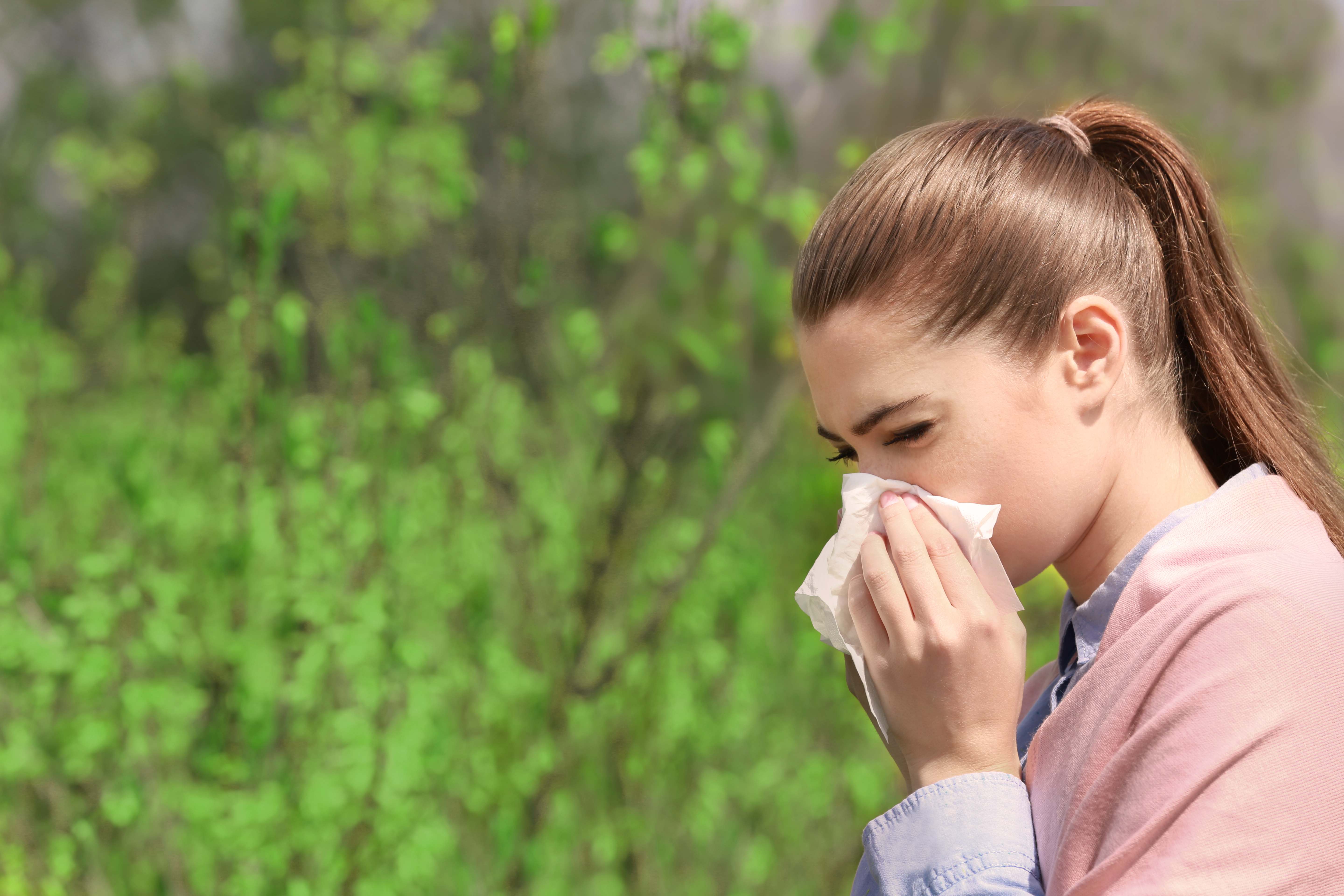 Sneezing young girl with tissue among blooming trees in park