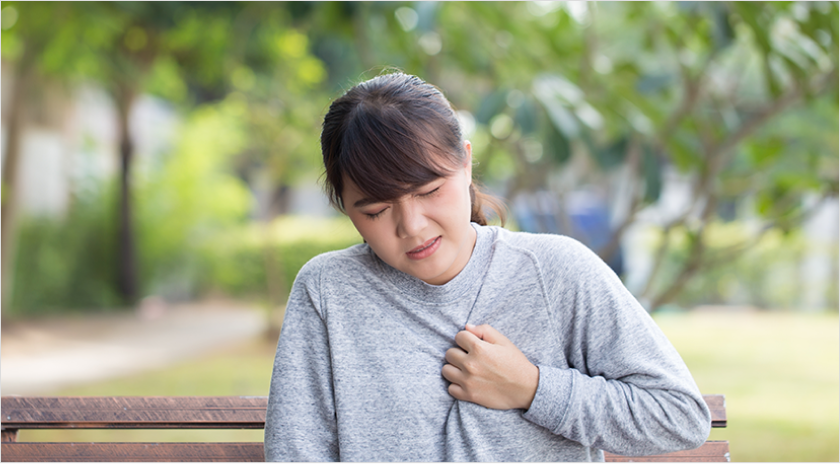 Woman sitting on a park bench hold her hand to her chest with look of pain on her face