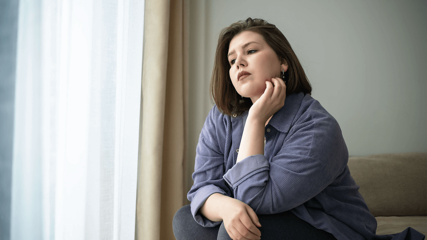 plus size woman sitting on bed with solemn expression