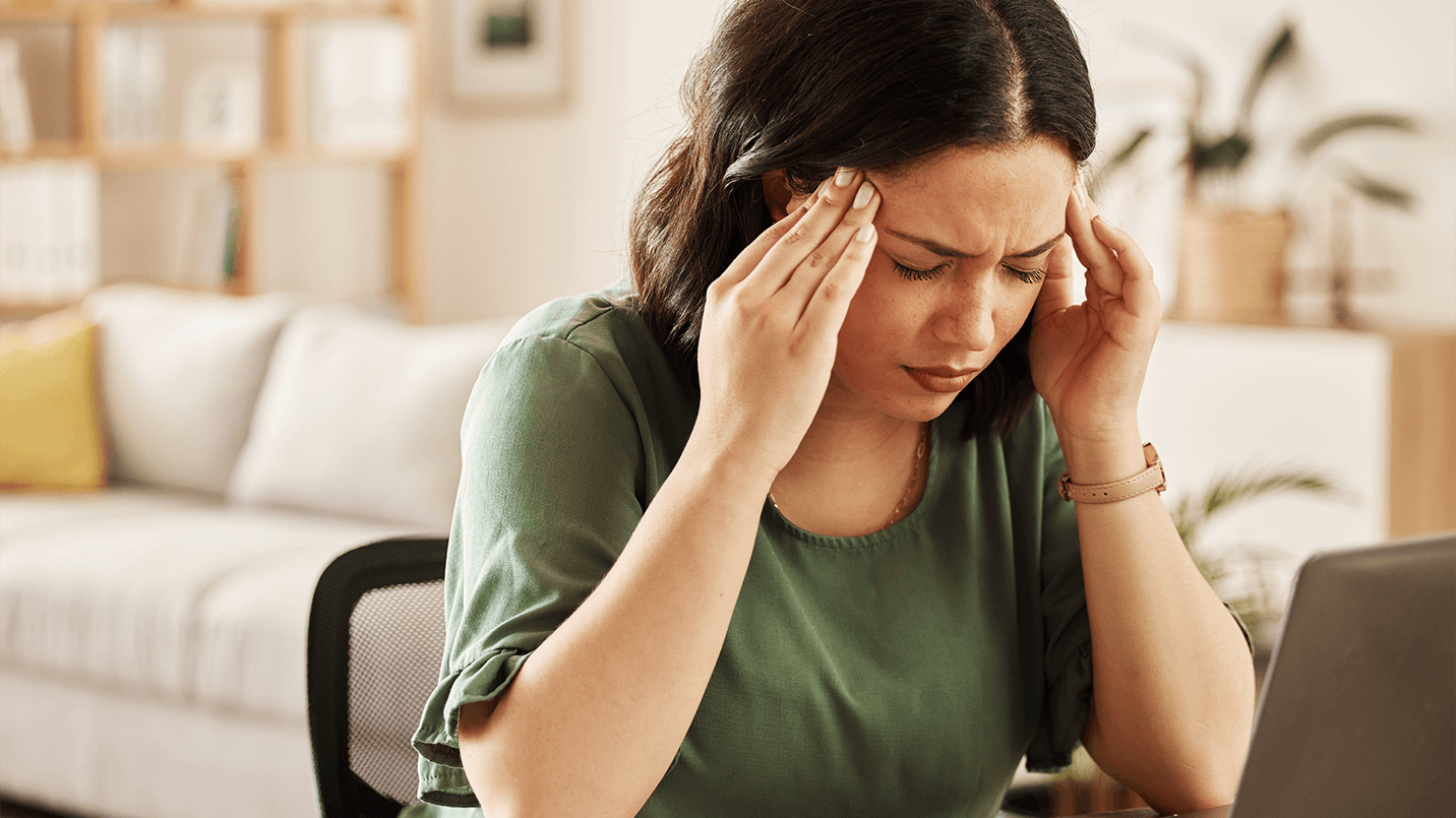 brown haired young woman in pain from headache, rubbing her temples to find relief