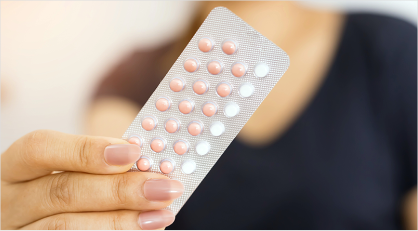 Up-close shot of woman's hands holding a packet of birth control pills towards the camera