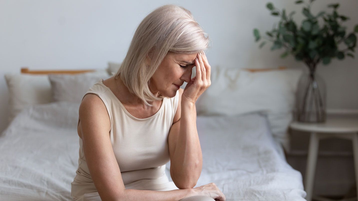 older woman sitting on bed and rubbing her forehead to relieve discomfort