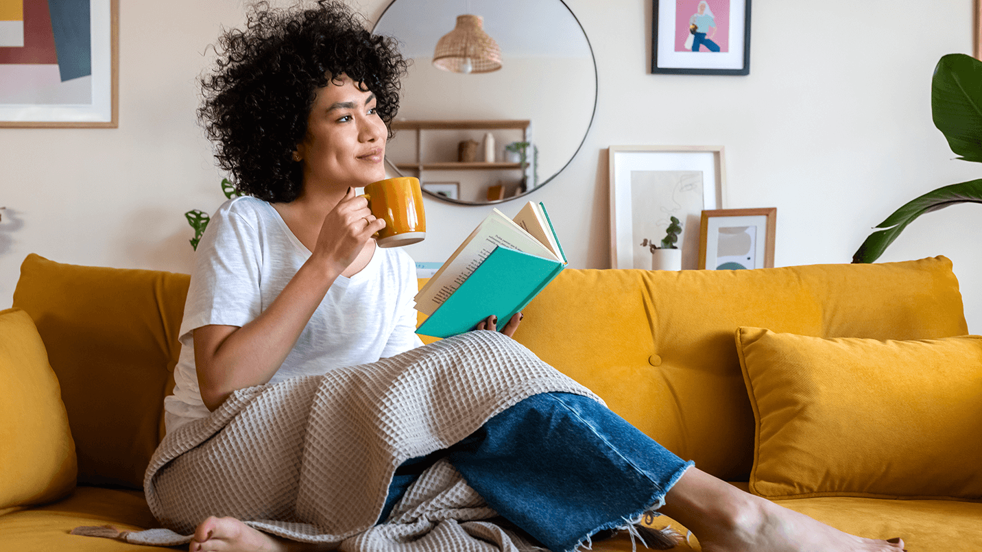 woman reading and enjoying a cup of coffee on a yellow couch