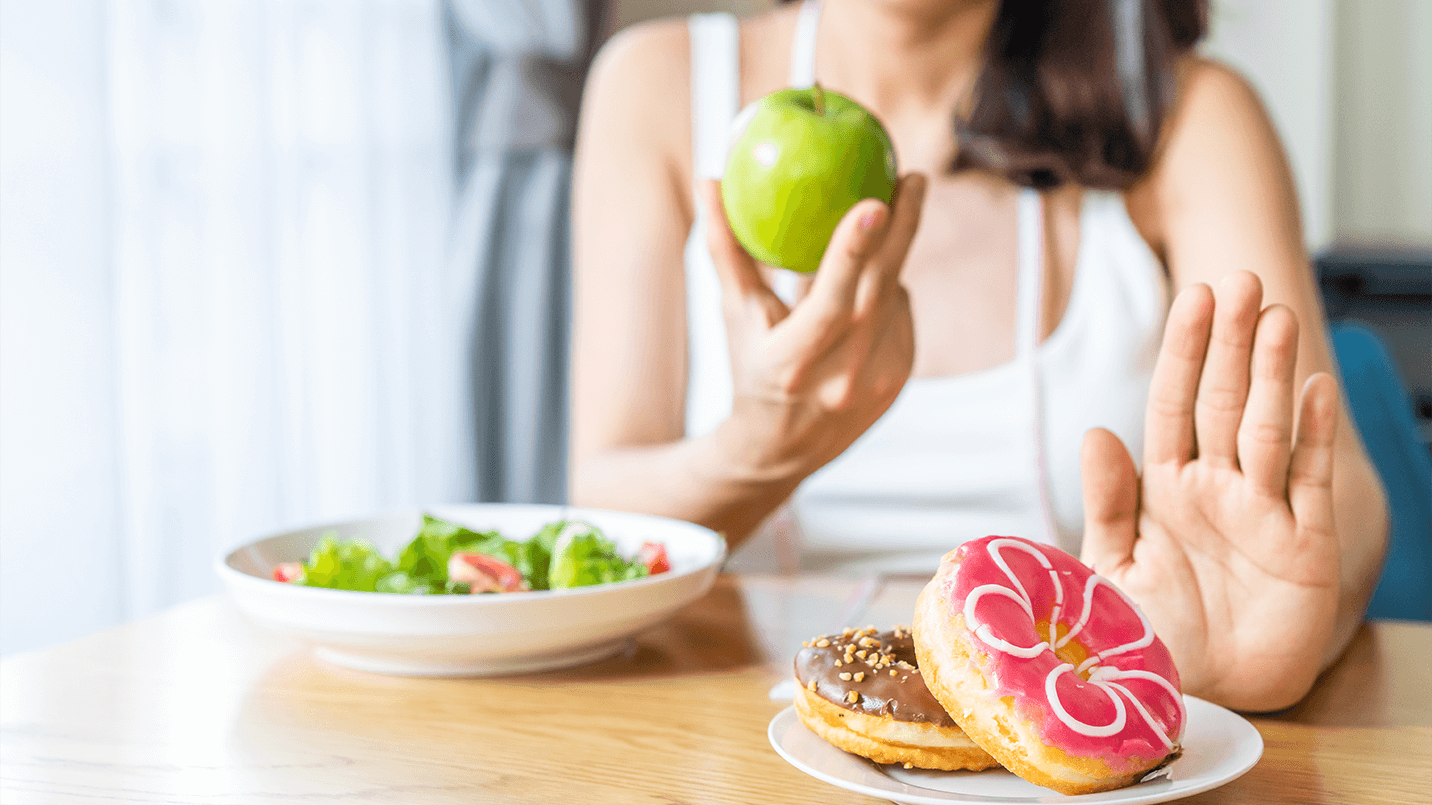 woman holding green apple and rejecting donuts