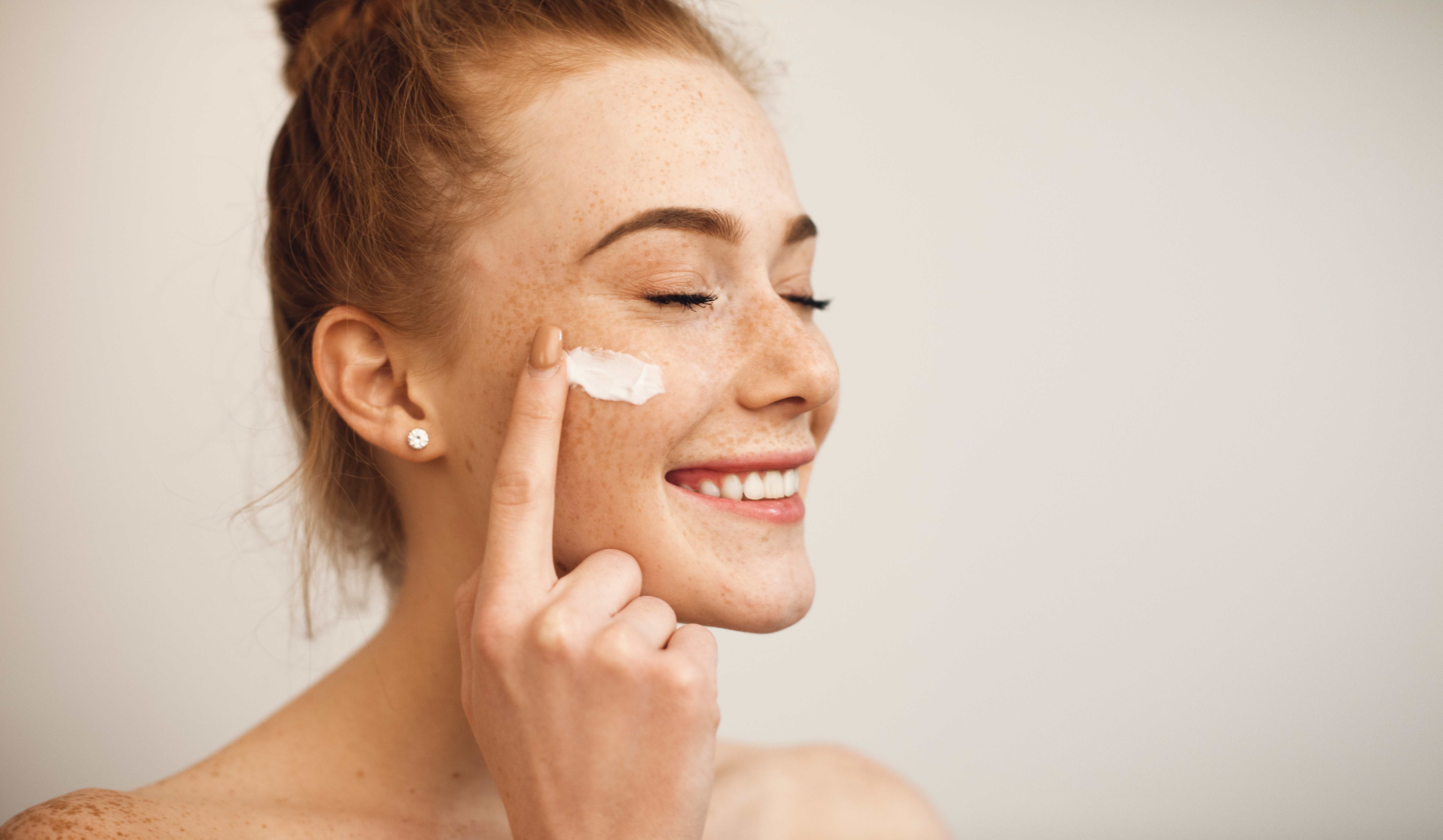 Woman smiling and spreading a skincare product onto her face with her finger