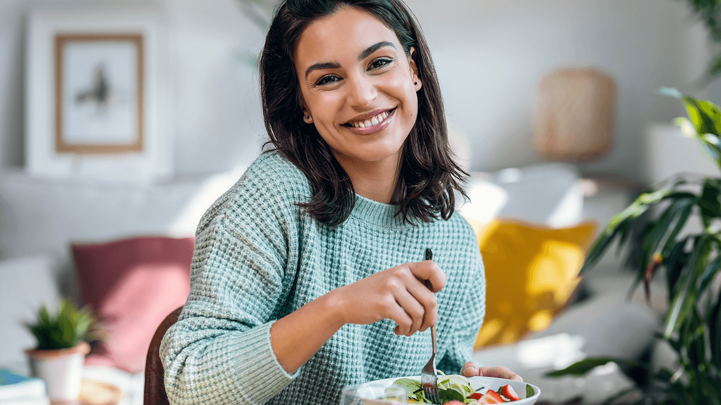 woman eating a health salad and smiling at the camera