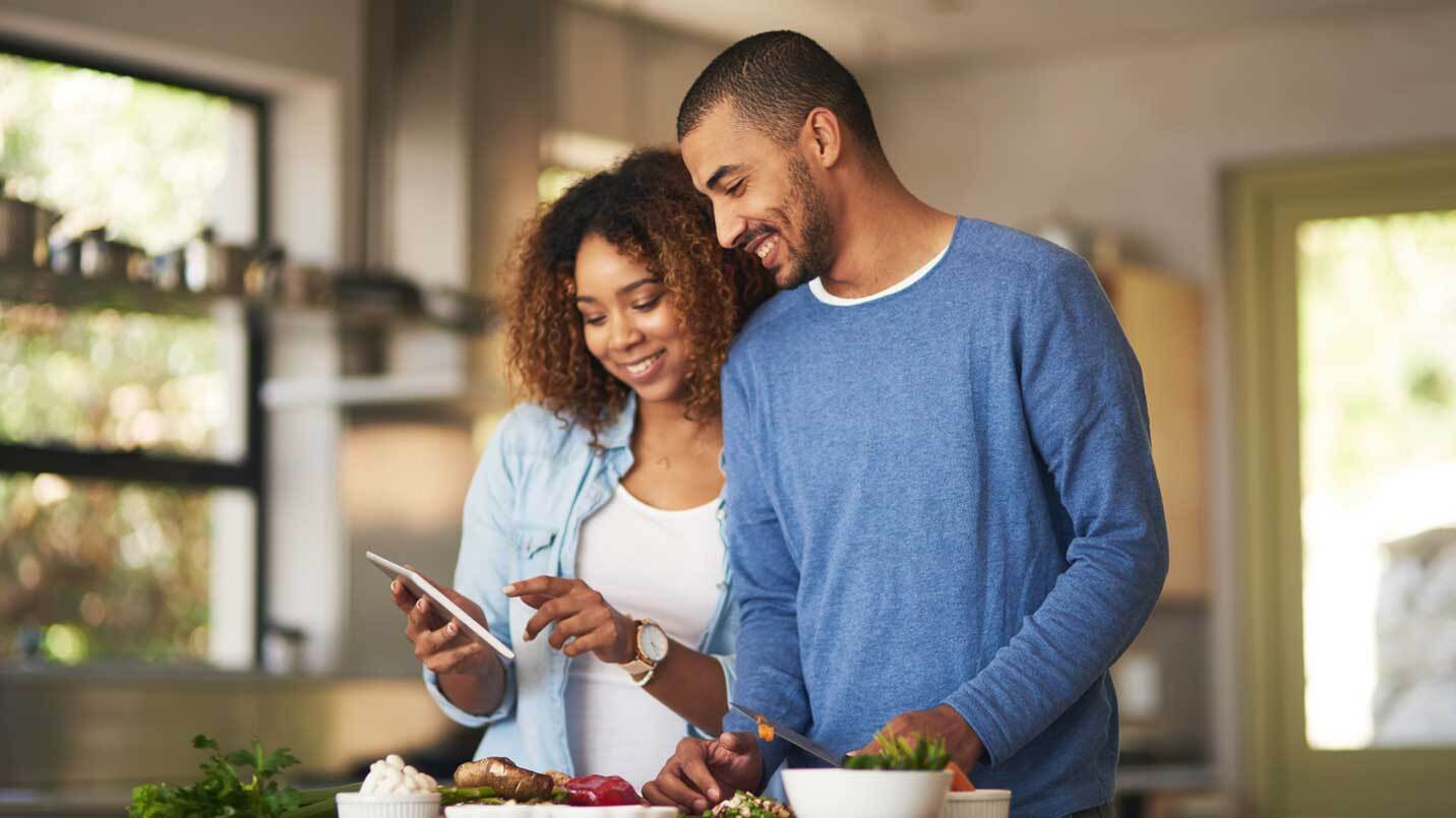 man and woman cooking a healthy lunch with each other and smiling