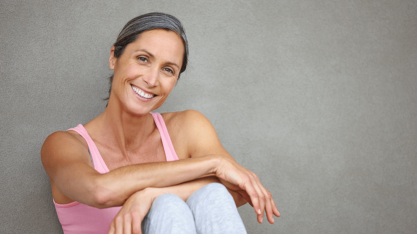 woman in pink tank top sitting down and leaning on a wall, smiling at the camera