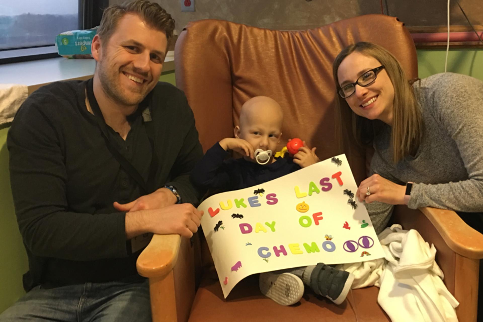 Luke in the hospital with his parents and a sign saying "Luke's last day of chemo"