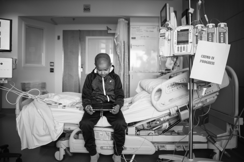 Kid alone in the hospital playing by himself with a "Chemo In Process" sign next to him