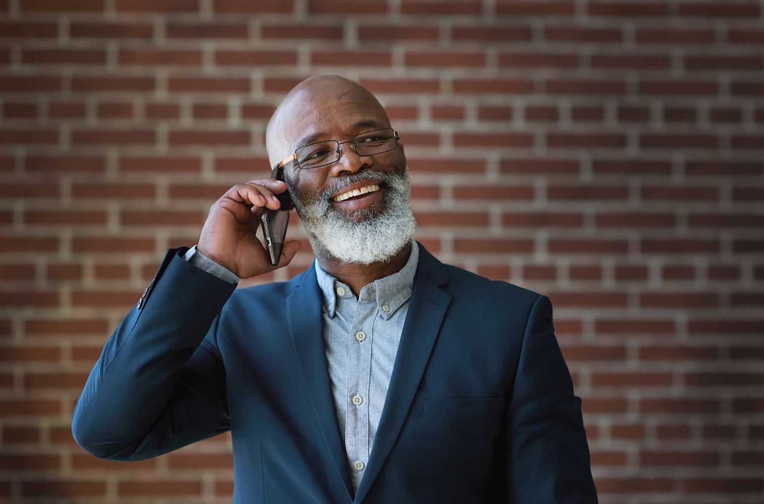 Older man wearing a suit on the phone using the Financial Center voice responsive system standing in front of a brick wall