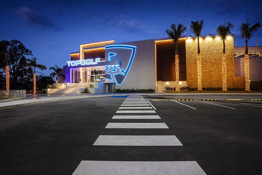 Topgolf Gold Coast venue at night with blue lights and palm trees.