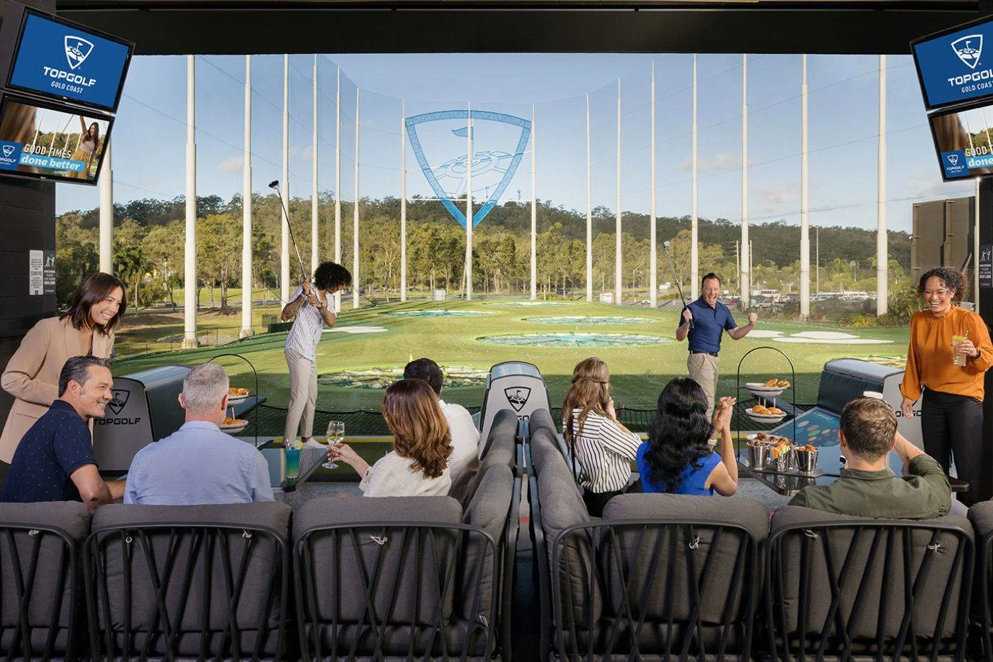 A group of people sitting in a Topgolf venue watching a golf game.