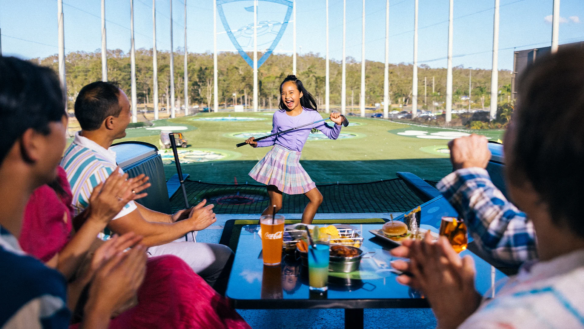 A group of people sitting at a table at Topgolf Gold Coast, enjoying their game and sharing delicious food and drinks.