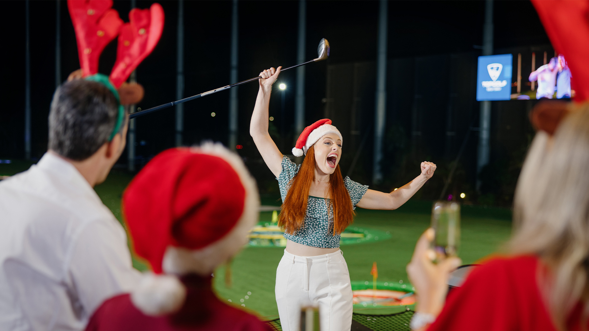 A group of people playing golf in Santa hats at a Christmas party at Topgolf Gold Coast.