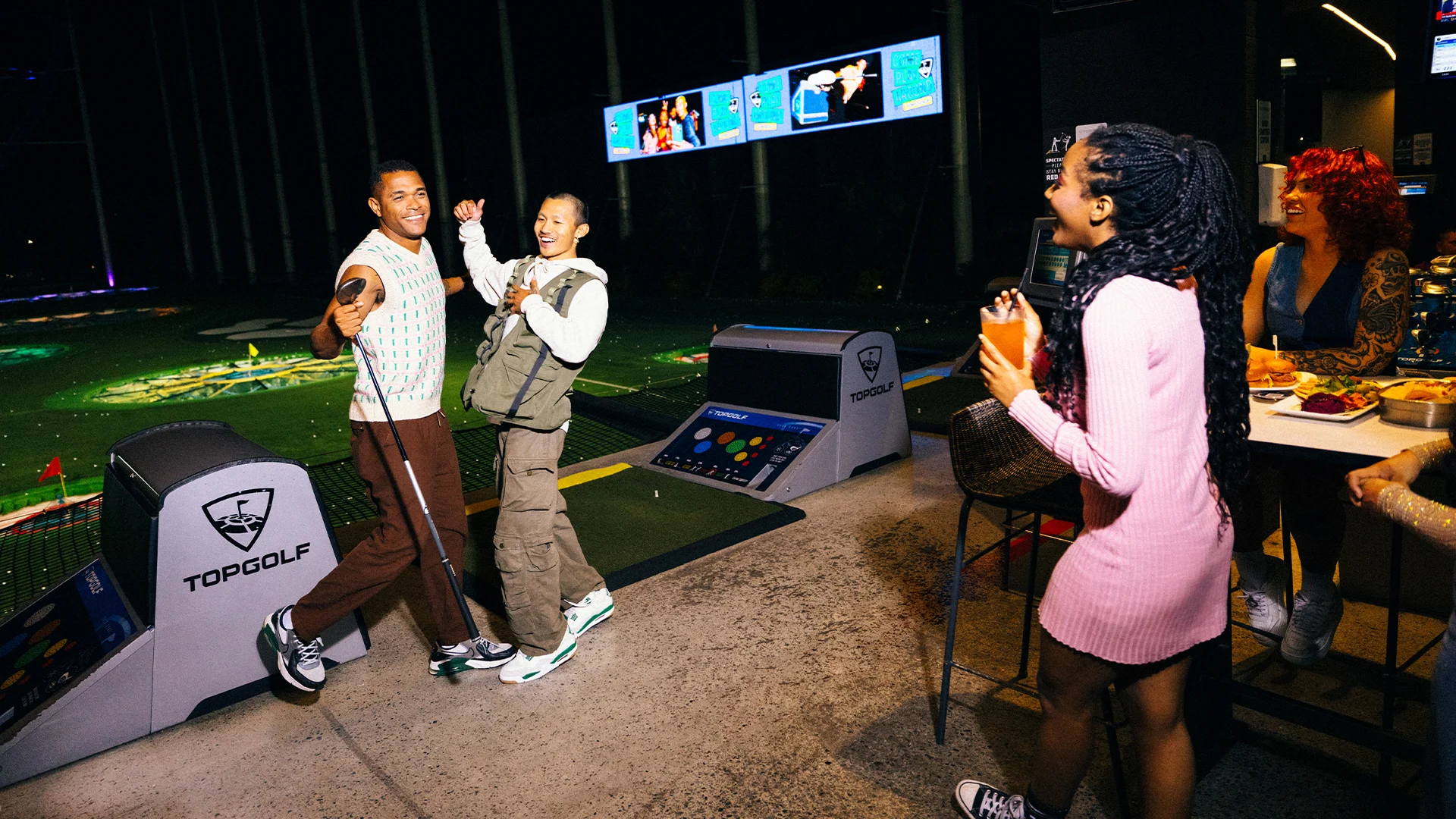 A group of people playing a game of golf at night during a Topgolf event.