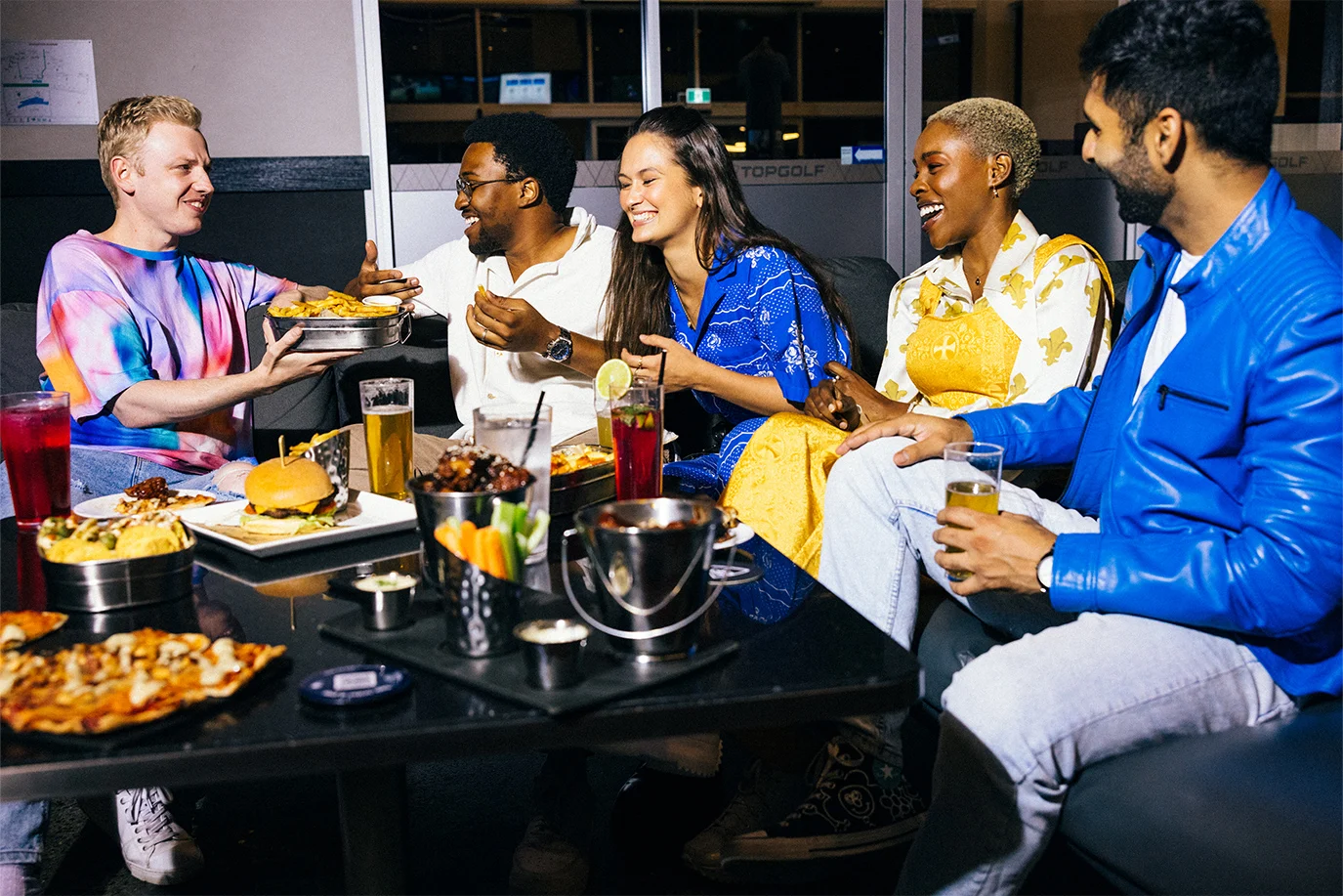 Five people sitting around a table with food and drinks, smiling and enjoying each other's company.