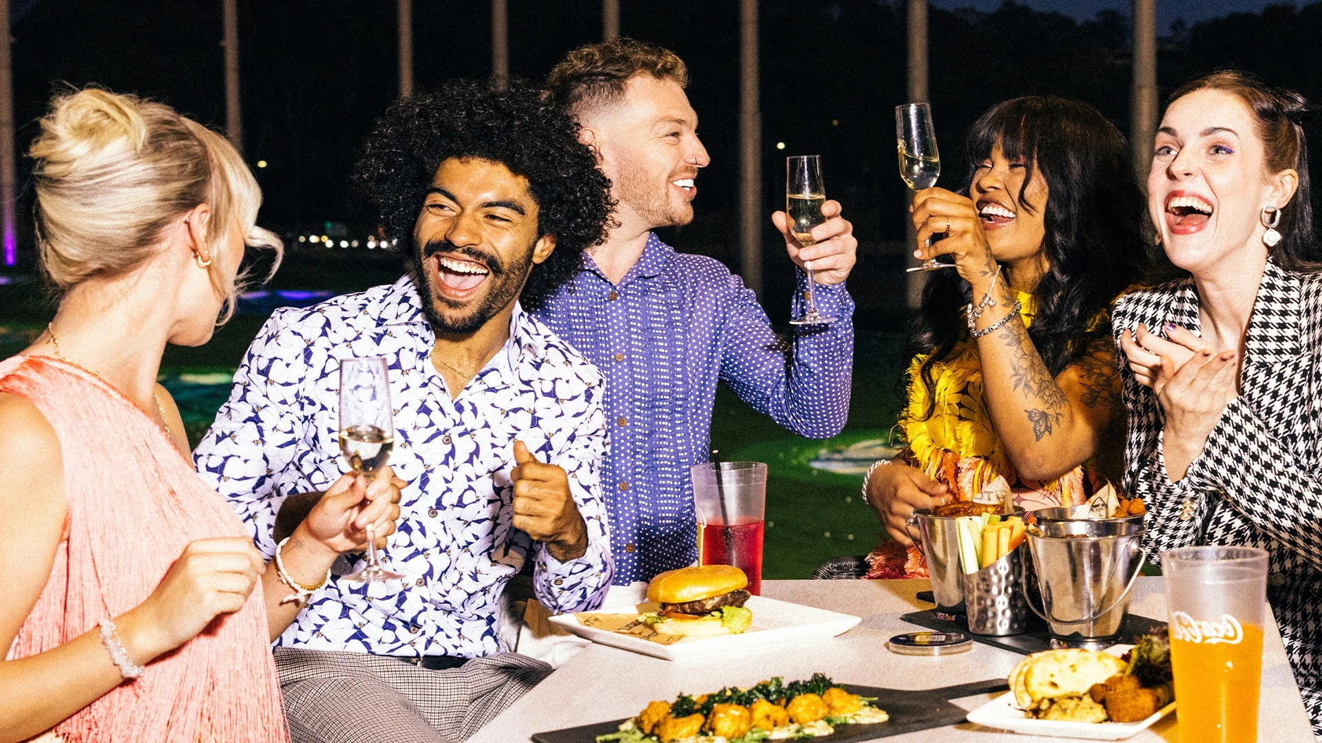 A group of people are sharing delicious food and drinks at Topgolf Gold Coast.