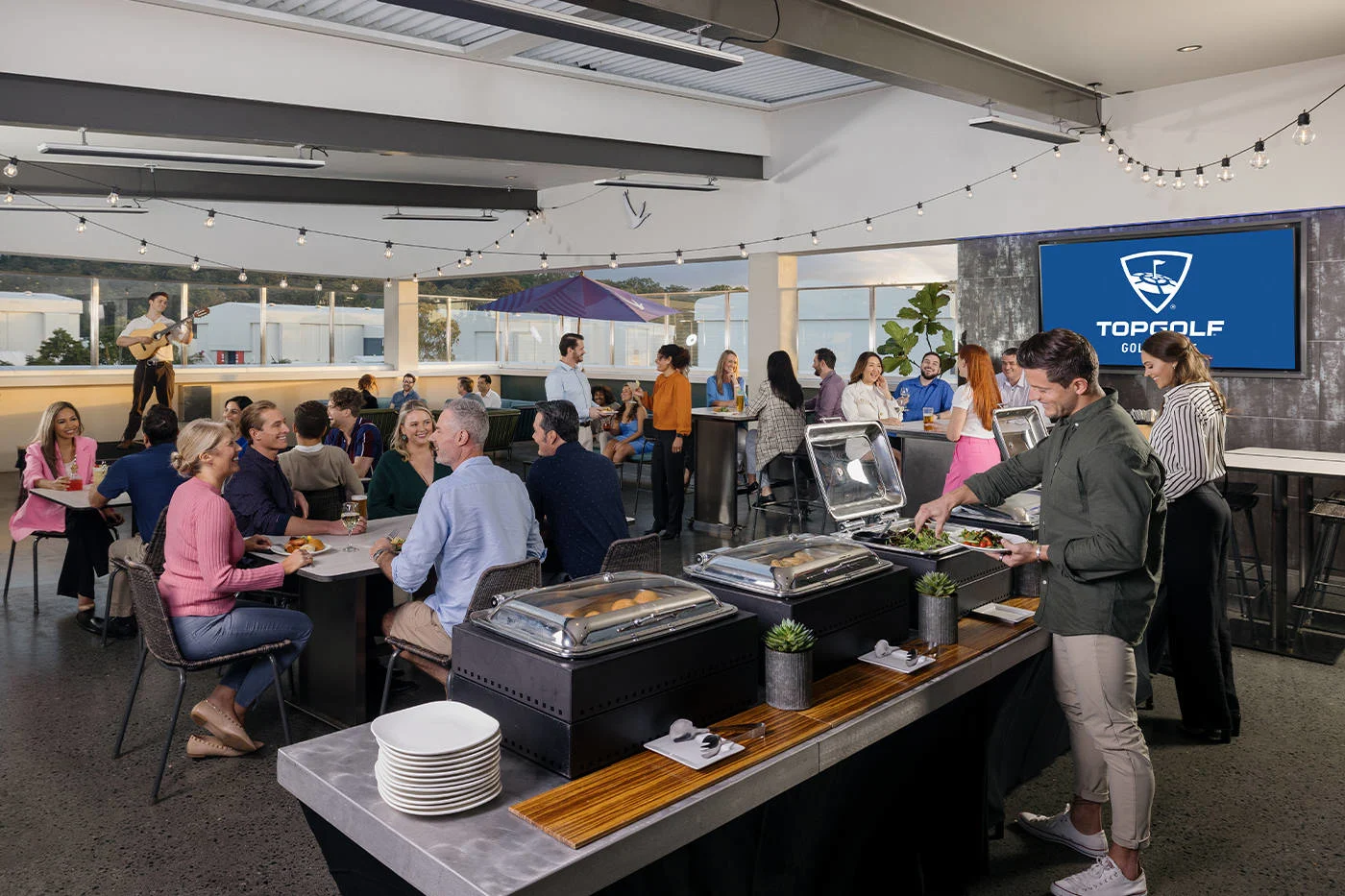 A group of people sharing delicious food and listening to live music at an event hosted at Topgolf Gold Coast.