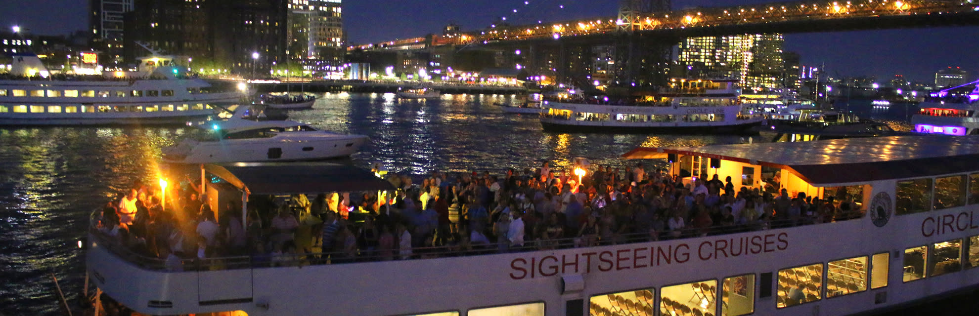 Guests enjoying a party on a Circle Line boat at night, sailing by the NYC skyline.