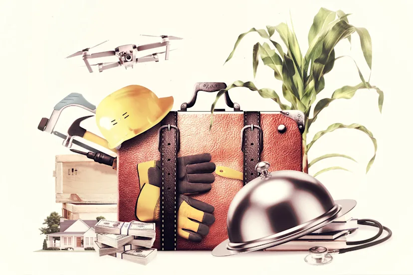 This image is a conceptual collage centered around a large brown leather briefcase, symbolizing work, business, and professional services. Arranged around the briefcase are objects representing a wide range of industries and occupations.
In the foreground, a yellow construction hard hat rests on the briefcase alongside a hammer, protective work gloves, and a utility tool. Above the briefcase, a drone is shown in flight. On the right side, tall green corn stalks emerge from behind the briefcase. In front of the corn plant is a silver serving dome. Nearby, a stethoscope and books. On the left side, a wooden crate, a small house, and stacks of cash are visible.