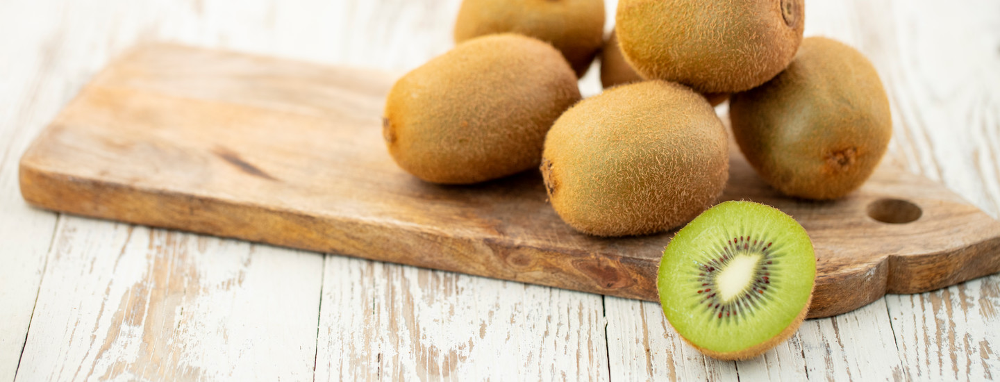 Tuoreita kiivejä puisella leikkuulaudalla. Edustalla on puoliksi leikattu kiivi. K-Ruoka raaka-aine.