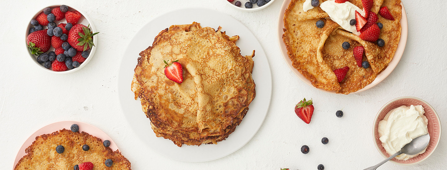 Muurinpohjalettuja valkoisella lautasella marjojen ja kermavaahdon kanssa.