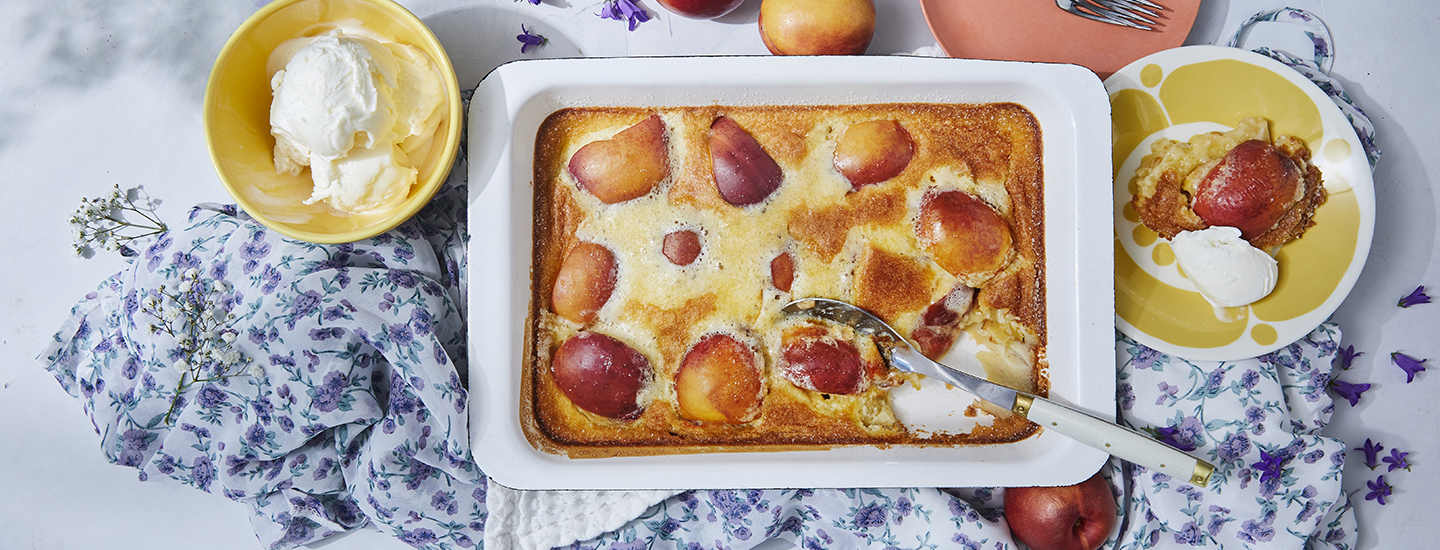 Clafoutis eli ranskalaista pannukakkua valkoisessa uunivuoassa. Pannukakun seassa on nektariinipaloja ja pannukakku on vanukasmainen. K-Ruoka jälkiruokaresepti.