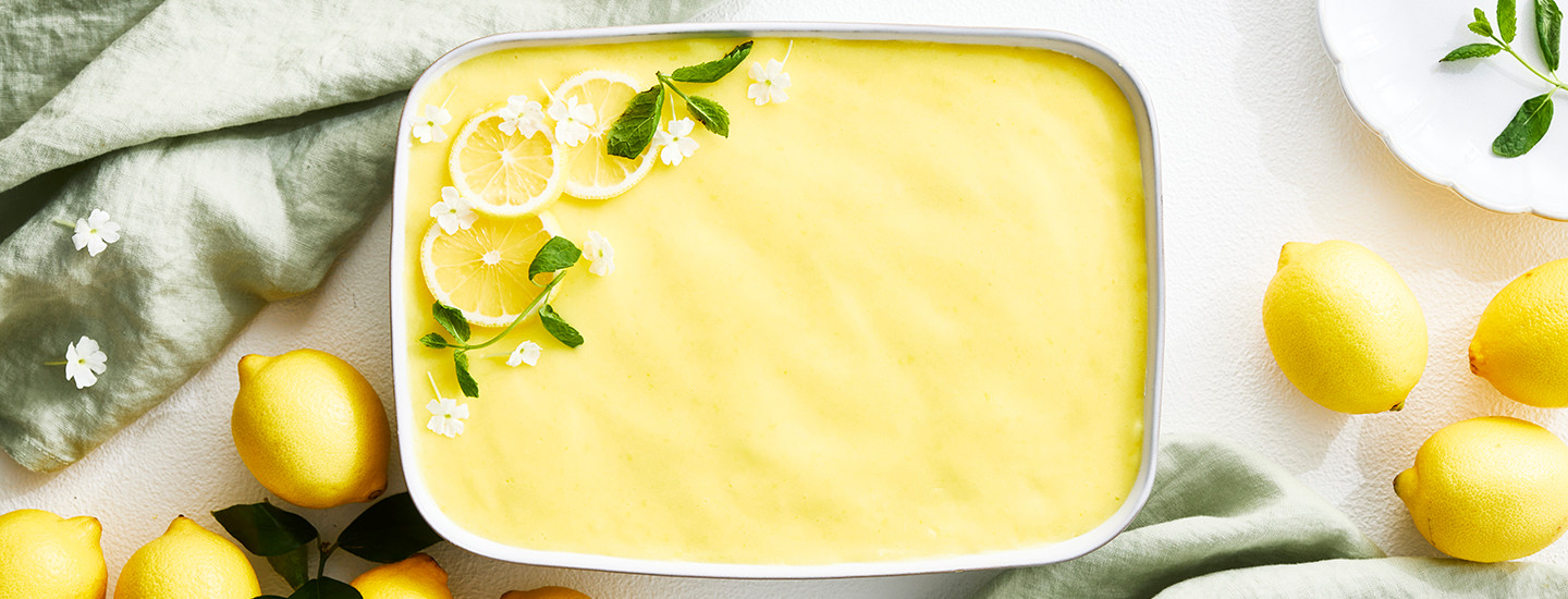 Sitruunatiramisua valkoisessa vuoassa. Tiramisu on päällystetty keltaisella lemon curdilla ja koristeltu sitruunaviipaleilla sekä mintunlehdillä. K-Ruoka jälkiruokaresepti.