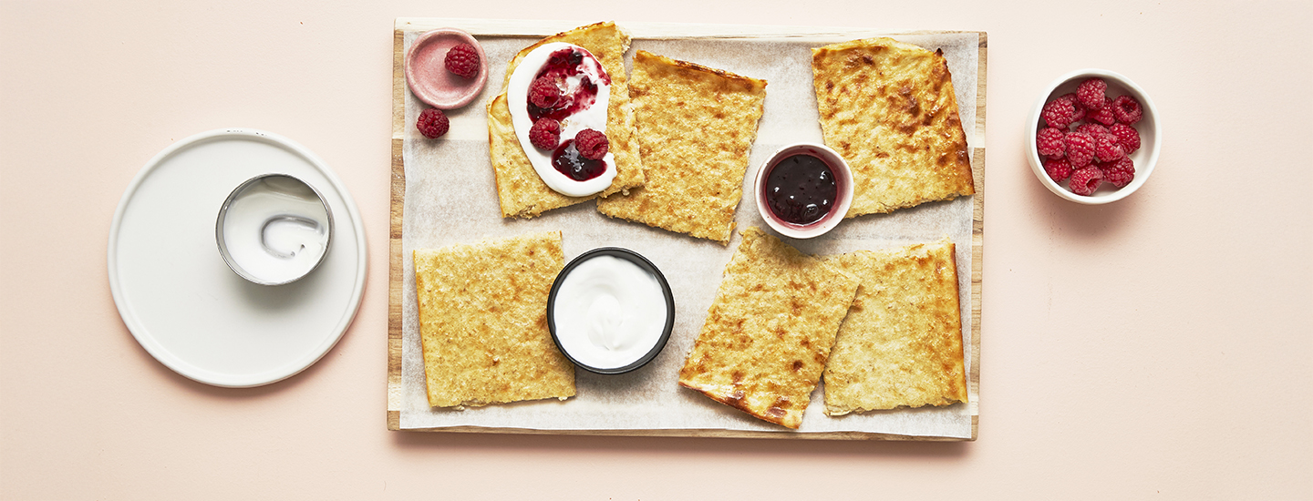 Kaurapannarin paloja puisella alustalla leivinpaperin päällä. Yhden pannaripalan päällä on kermavaahtoa ja marjoja. K-Ruoka jälkiruokaresepti.