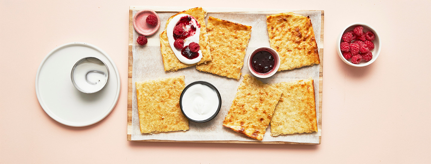 Kaurapannarin paloja puisella alustalla leivinpaperin päällä. Yhden pannaripalan päällä on kermavaahtoa ja marjoja. K-Ruoka jälkiruokaresepti.