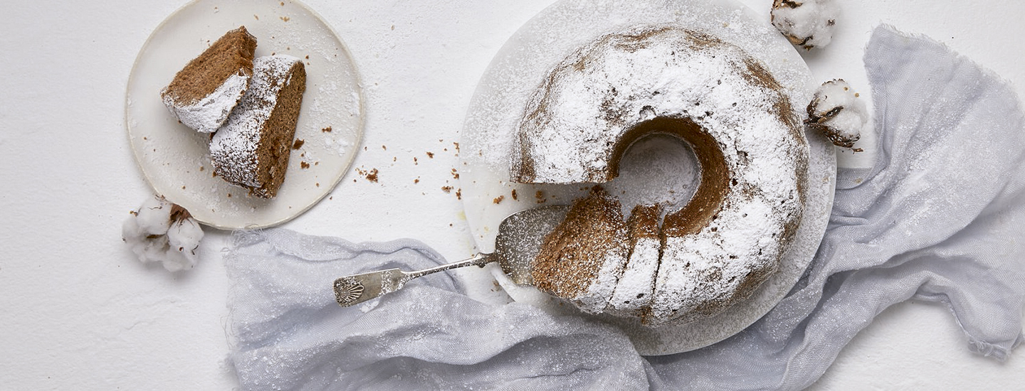 Gluteenitonta maustekakkua valkoisella lautasella. Maustekakusta on leikattu siivuja pienemmälle valkoiselle lautaselle. Maustekakun päälle on ripoteltu tomusokeria. K-Ruoka gluteeniton leivontaresepti.