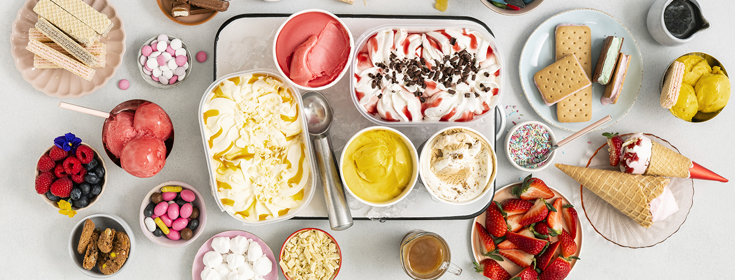 Erilaisia jäätelöpakkauksia ja yksittäisiä jäätelötuutteja pöydällä ja tarjottimilla. 