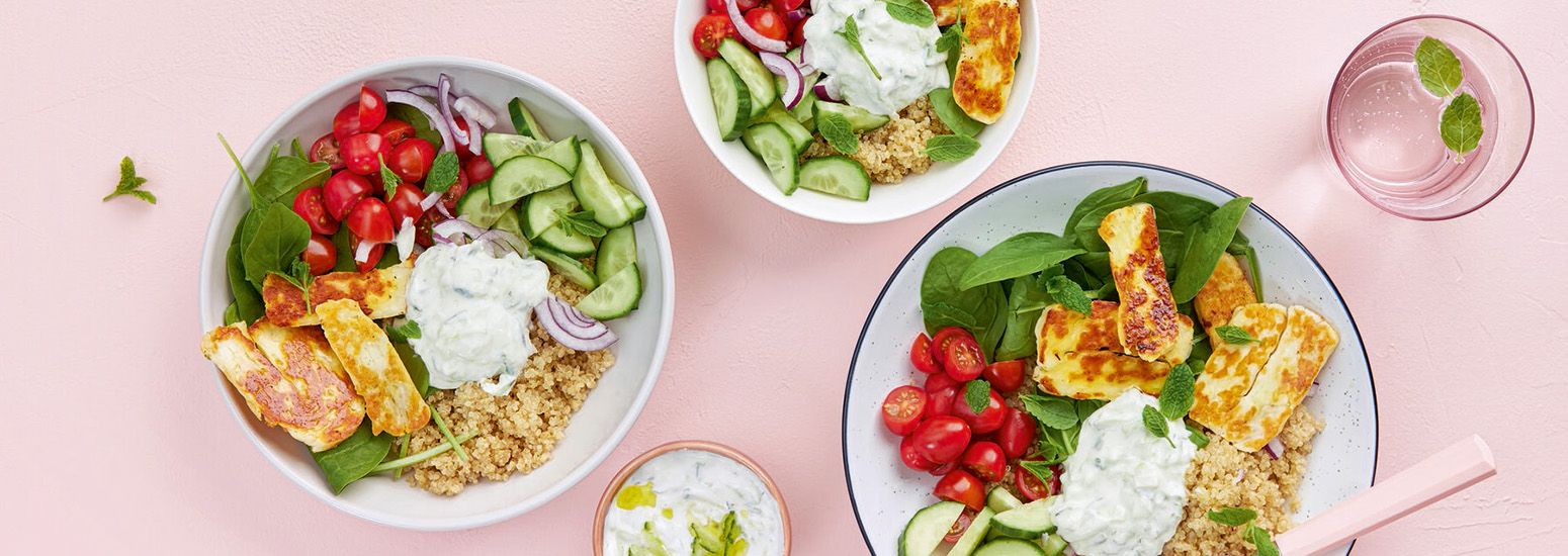 Halloumi-bowl. K-Ruoan reseptin kuva, jossa lautasia vaaleapunaisella taustalla. Salaatissa muun muassa halloumia, kurkkua ja kirsikkitomaatteja.